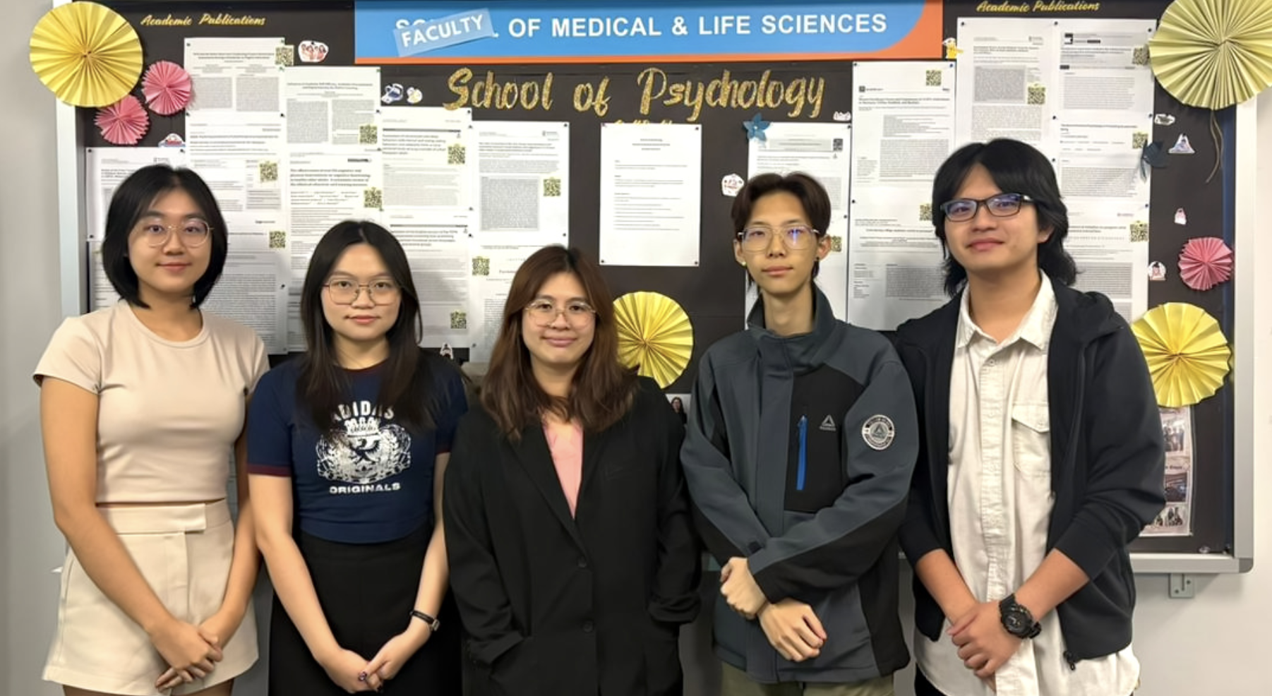 Dr Mah and the founding research assistants outside the School of Psychology noticeboard